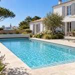 Piscine rénovée avec margelles en pierre claire et terrasse devant une maison en Charente-Maritime